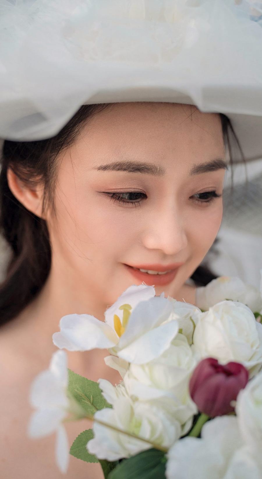 她捧着白色的花束，低头笑